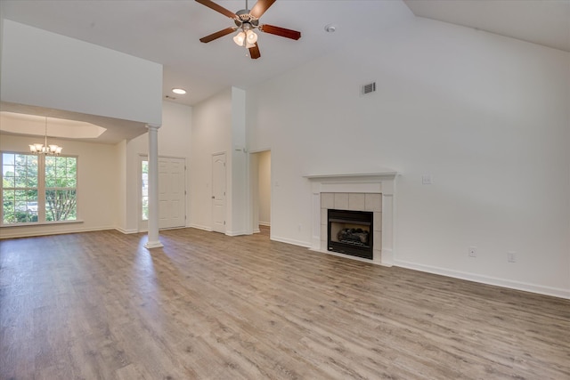 unfurnished living room featuring ceiling fan, wood finished floors, a tile fireplace, high vaulted ceiling, and a chandelier