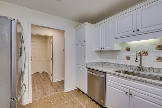 kitchen with stainless steel appliances, a sink, white cabinets, baseboards, and tasteful backsplash