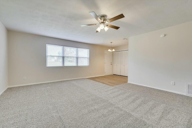 empty room with light colored carpet and ceiling fan with notable chandelier