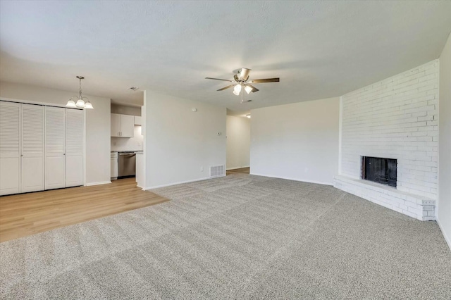 unfurnished living room with ceiling fan with notable chandelier, a fireplace, and light carpet