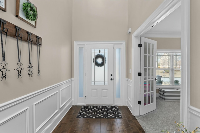 entrance foyer featuring wainscoting, dark wood-style floors, ornamental molding, french doors, and a decorative wall