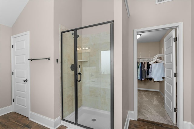 full bathroom with wood finished floors, a shower stall, a walk in closet, and baseboards