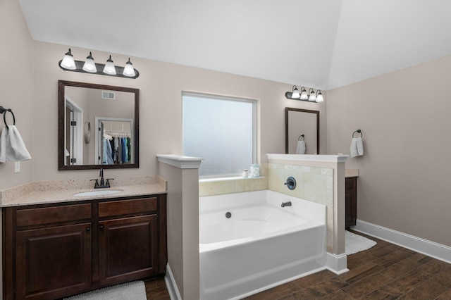 bathroom featuring wood finished floors, vanity, baseboards, vaulted ceiling, and a bath