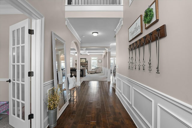 hallway featuring a decorative wall, a wainscoted wall, coffered ceiling, dark wood finished floors, and crown molding