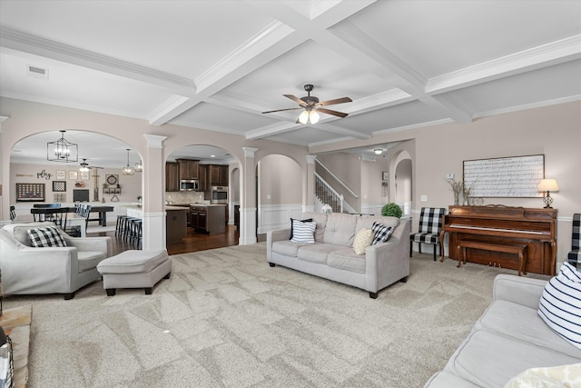 living area with ornate columns, arched walkways, beamed ceiling, and light colored carpet