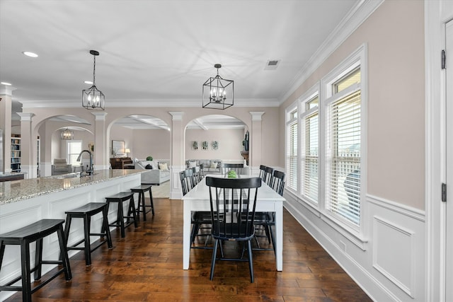 dining room featuring dark wood-style floors, a wainscoted wall, a healthy amount of sunlight, and ornamental molding