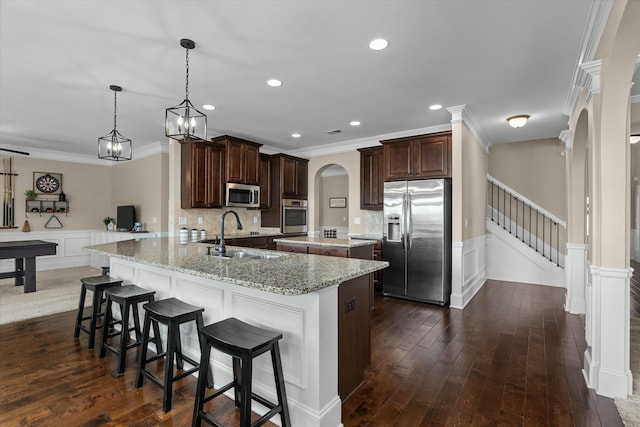 kitchen with arched walkways, dark brown cabinetry, a kitchen island, a sink, and appliances with stainless steel finishes