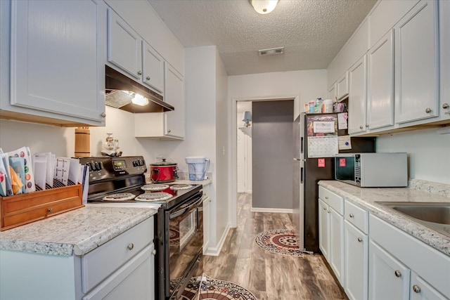 2382 Patrick Ave, Hephzibah, GA 30815 - kitchen with black range with electric cooktop, white microwave, under cabinet range hood, light wood-style floors, and light countertops