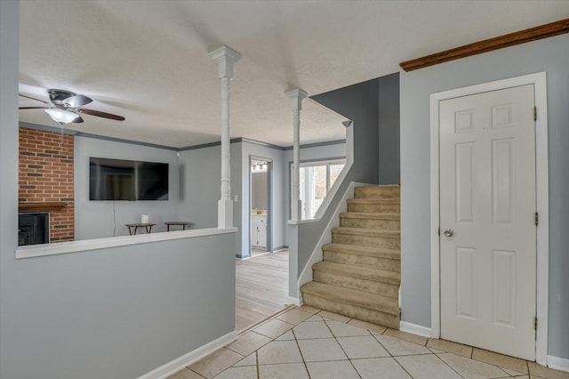 stairway featuring tile patterned flooring, crown molding, ceiling fan, a fireplace, and a textured ceiling