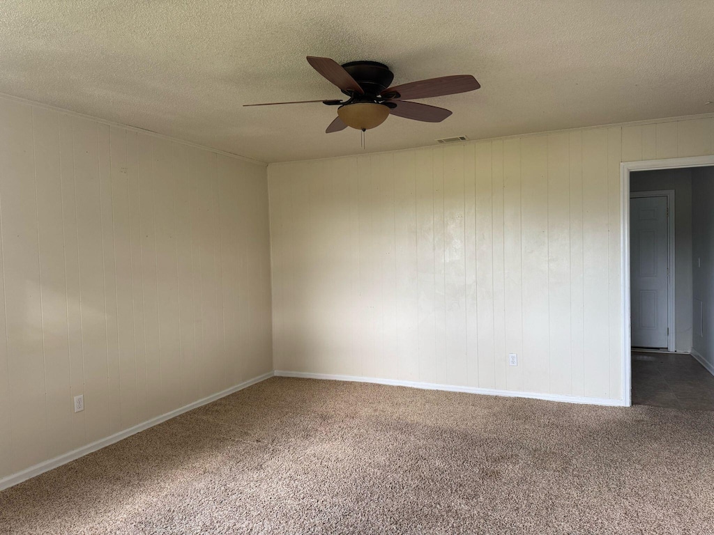 carpeted spare room featuring ceiling fan, baseboards, a textured ceiling, and visible vents