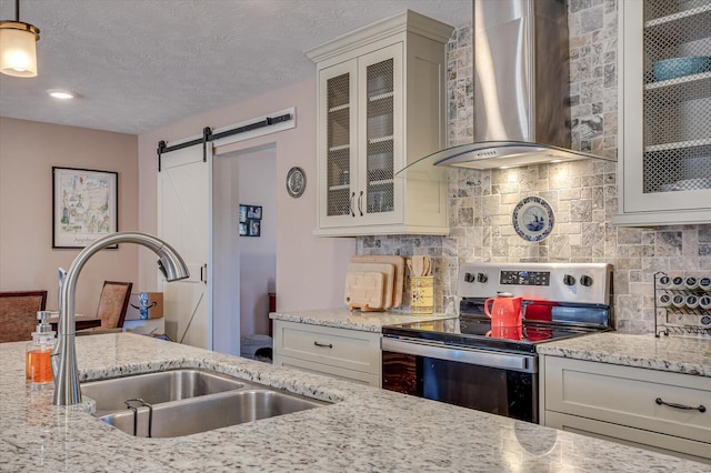 kitchen featuring a barn door, electric stove, light stone countertops, wall chimney exhaust hood, and sink