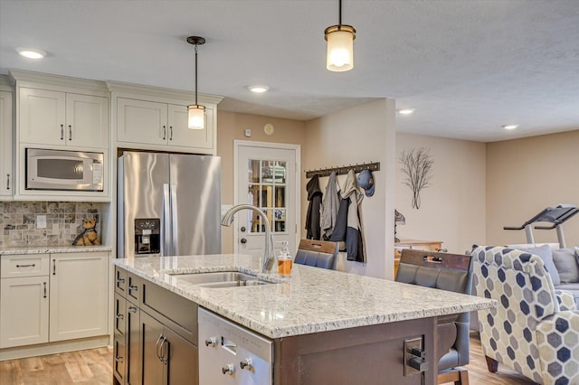 kitchen with decorative light fixtures, sink, appliances with stainless steel finishes, and a kitchen island with sink