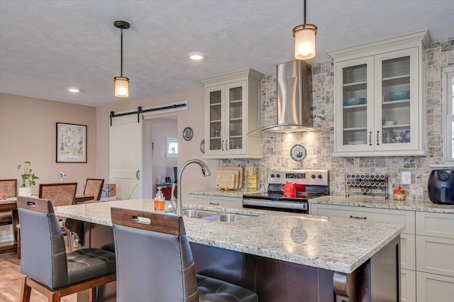 kitchen with a kitchen bar, a barn door, stainless steel electric range, and wall chimney range hood