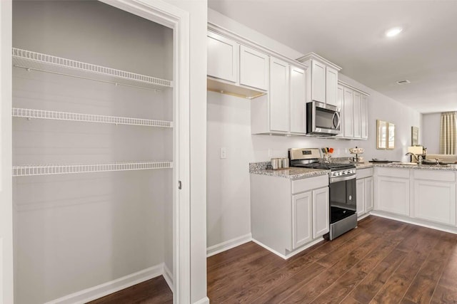 kitchen featuring stainless steel appliances, white cabinets, light stone countertops, and dark hardwood / wood-style floors