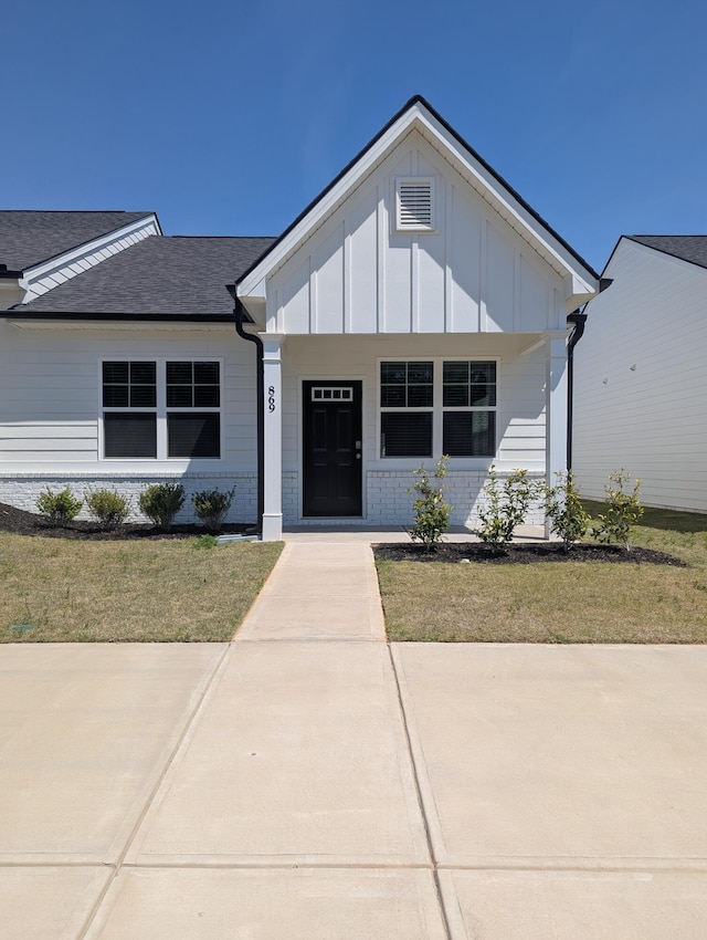 modern farmhouse with board and batten siding, brick siding, a porch, and a front lawn