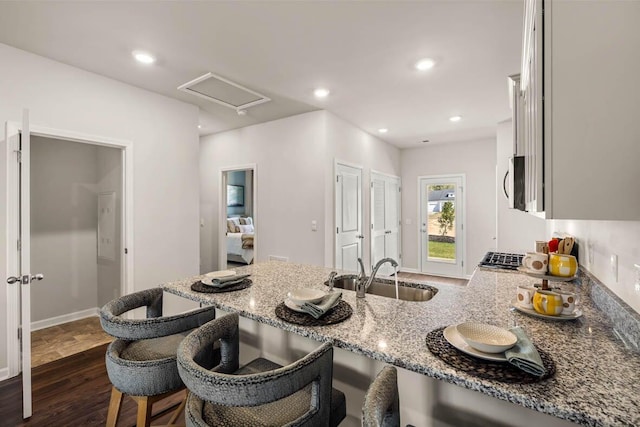 kitchen featuring light stone countertops, a kitchen bar, dark hardwood / wood-style flooring, white cabinets, and sink