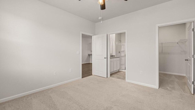 unfurnished bedroom featuring a closet, ensuite bath, ceiling fan, a walk in closet, and light colored carpet