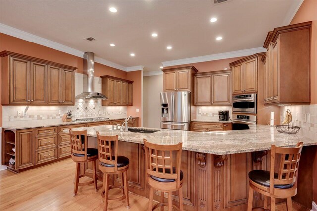 kitchen featuring light stone countertops, appliances with stainless steel finishes, sink, wall chimney range hood, and a breakfast bar area