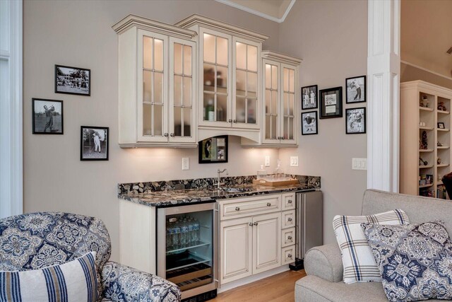 bar featuring sink, wine cooler, dark stone countertops, crown molding, and light wood-type flooring