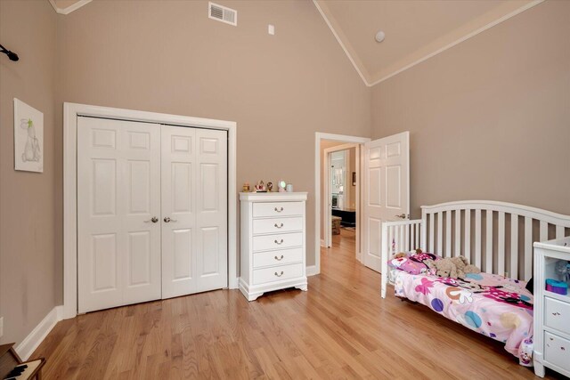 bedroom with light hardwood / wood-style flooring, crown molding, high vaulted ceiling, and a closet