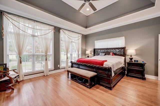 bedroom featuring light wood-type flooring, a tray ceiling, ceiling fan, and crown molding