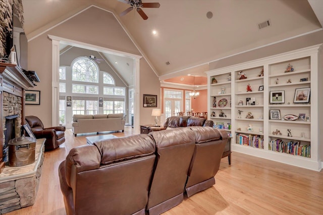 living room featuring a stone fireplace, a wealth of natural light, light hardwood / wood-style flooring, and ceiling fan with notable chandelier