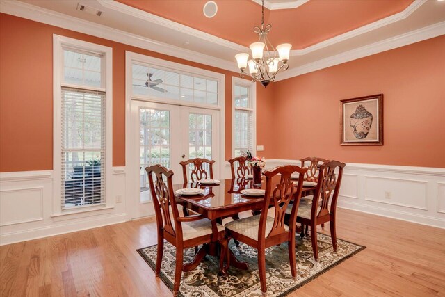 dining area featuring french doors, ceiling fan with notable chandelier, a raised ceiling, crown molding, and light hardwood / wood-style flooring