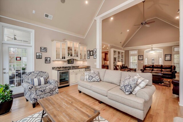 living room featuring high vaulted ceiling, ceiling fan with notable chandelier, light wood-type flooring, and beverage cooler