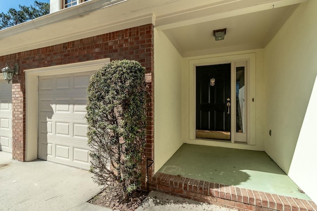 view of exterior entry with a garage, brick siding, and stucco siding