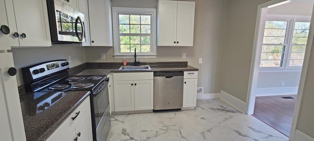 kitchen featuring white cabinetry, appliances with stainless steel finishes, sink, and dark stone counters