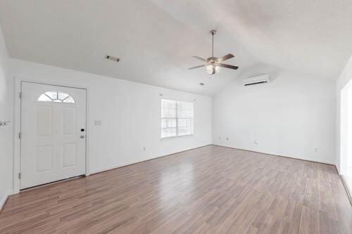 foyer entrance featuring ceiling fan, vaulted ceiling, a wall unit AC, and light hardwood / wood-style flooring