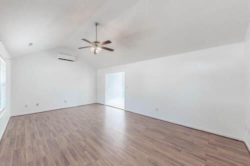 empty room featuring ceiling fan, wood-type flooring, a wall unit AC, and vaulted ceiling