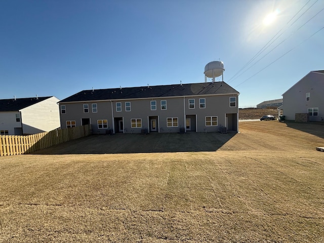 back of property with central AC unit, fence, and a lawn