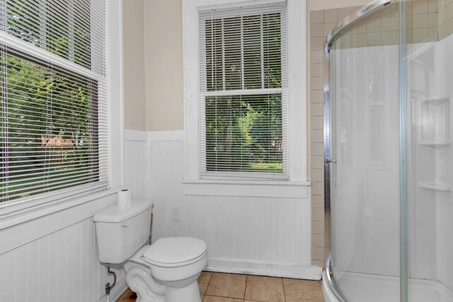 bathroom with tile patterned floors, toilet, and a shower with door