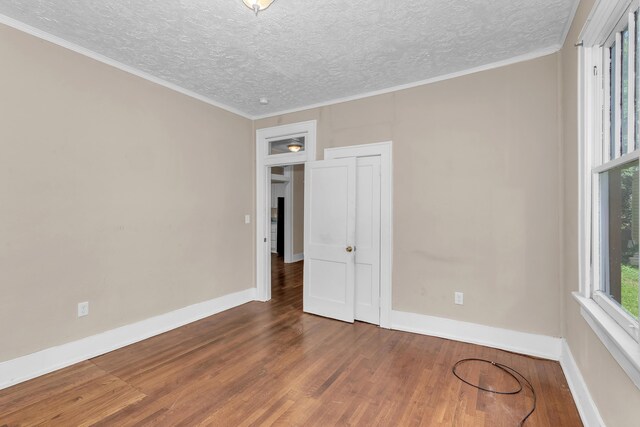 empty room with hardwood / wood-style floors, a textured ceiling, and crown molding