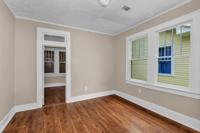 empty room with dark hardwood / wood-style flooring, a textured ceiling, and ornamental molding