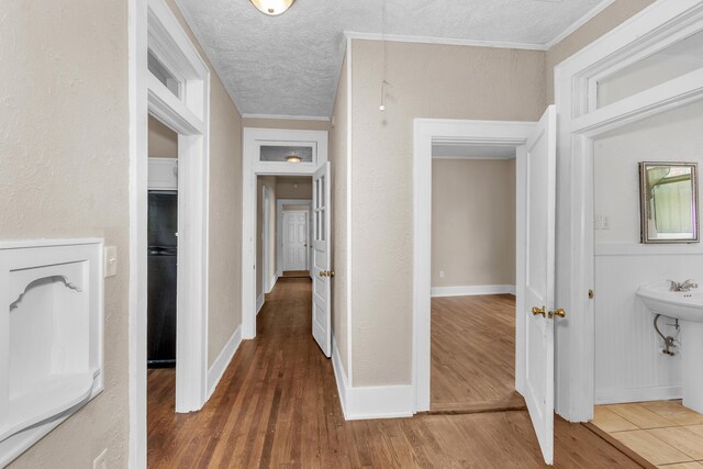 corridor with crown molding, a textured ceiling, and hardwood / wood-style flooring