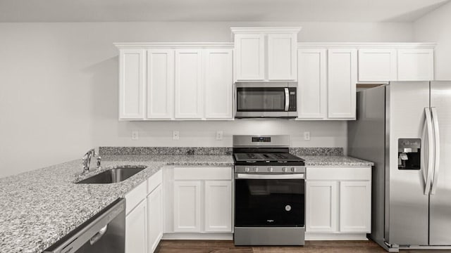 kitchen with dark wood-type flooring, sink, appliances with stainless steel finishes, light stone counters, and white cabinetry