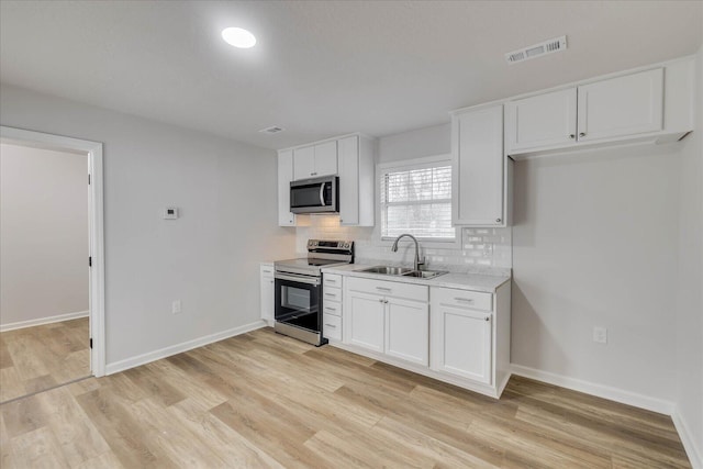 kitchen featuring light countertops, light wood-type flooring, decorative backsplash, appliances with stainless steel finishes, and a sink