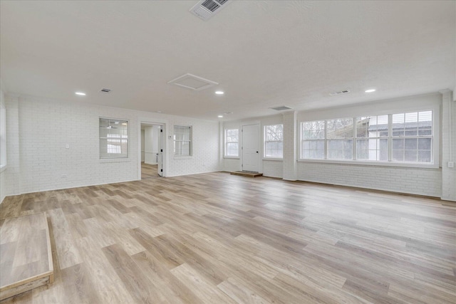 interior space featuring attic access, light wood-style floors, visible vents, and brick wall