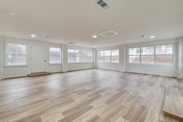 unfurnished living room with attic access, light wood finished floors, visible vents, and brick wall