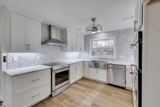 kitchen featuring appliances with stainless steel finishes, white cabinetry, sink, wall chimney exhaust hood, and light hardwood / wood-style flooring