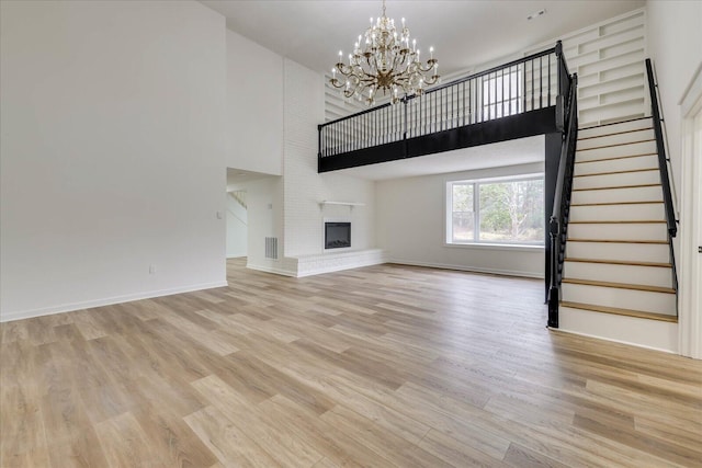 unfurnished living room featuring stairway, light wood-style floors, a high ceiling, and a notable chandelier