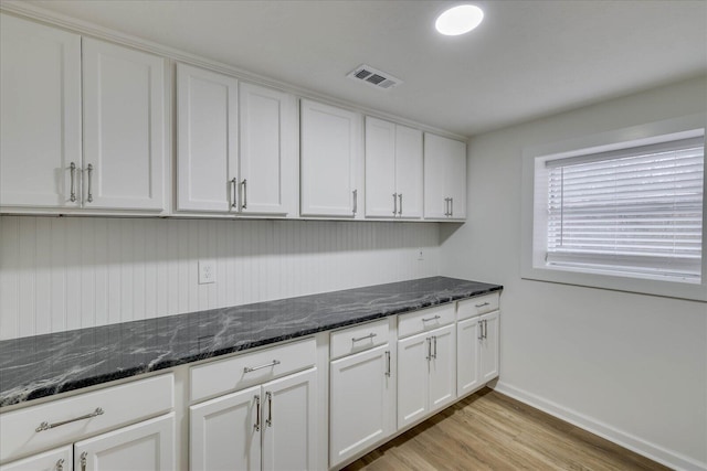 kitchen with visible vents, baseboards, light wood-style flooring, dark stone countertops, and white cabinetry