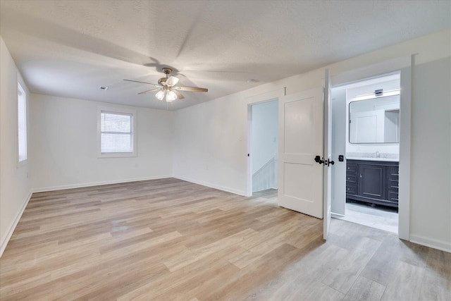 empty room with a ceiling fan, baseboards, light wood finished floors, and a textured ceiling