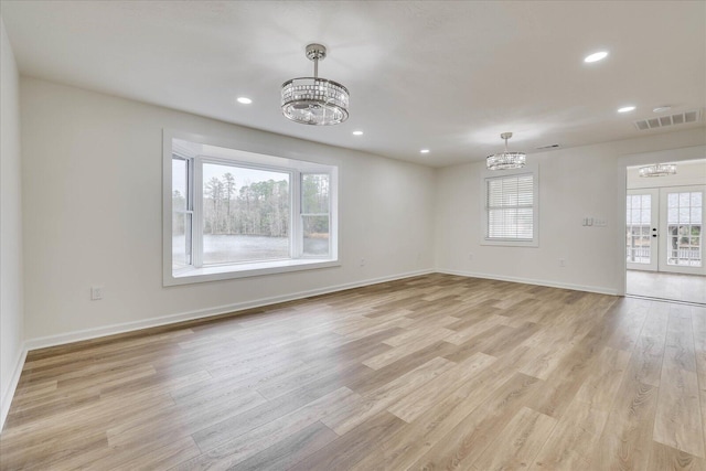 spare room with visible vents, plenty of natural light, an inviting chandelier, and light wood finished floors