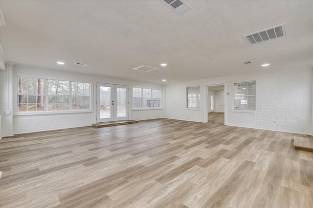 unfurnished living room featuring light wood finished floors, visible vents, brick wall, and french doors