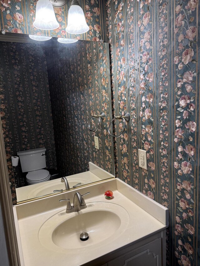bathroom featuring vanity, toilet, and wallpapered walls