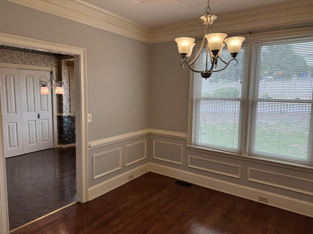 unfurnished dining area featuring an inviting chandelier, crown molding, wainscoting, and visible vents