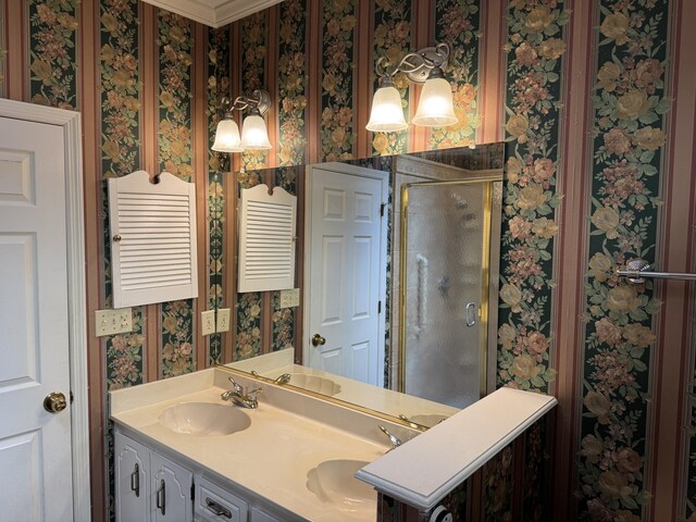 bathroom featuring crown molding, double vanity, wallpapered walls, a sink, and a stall shower